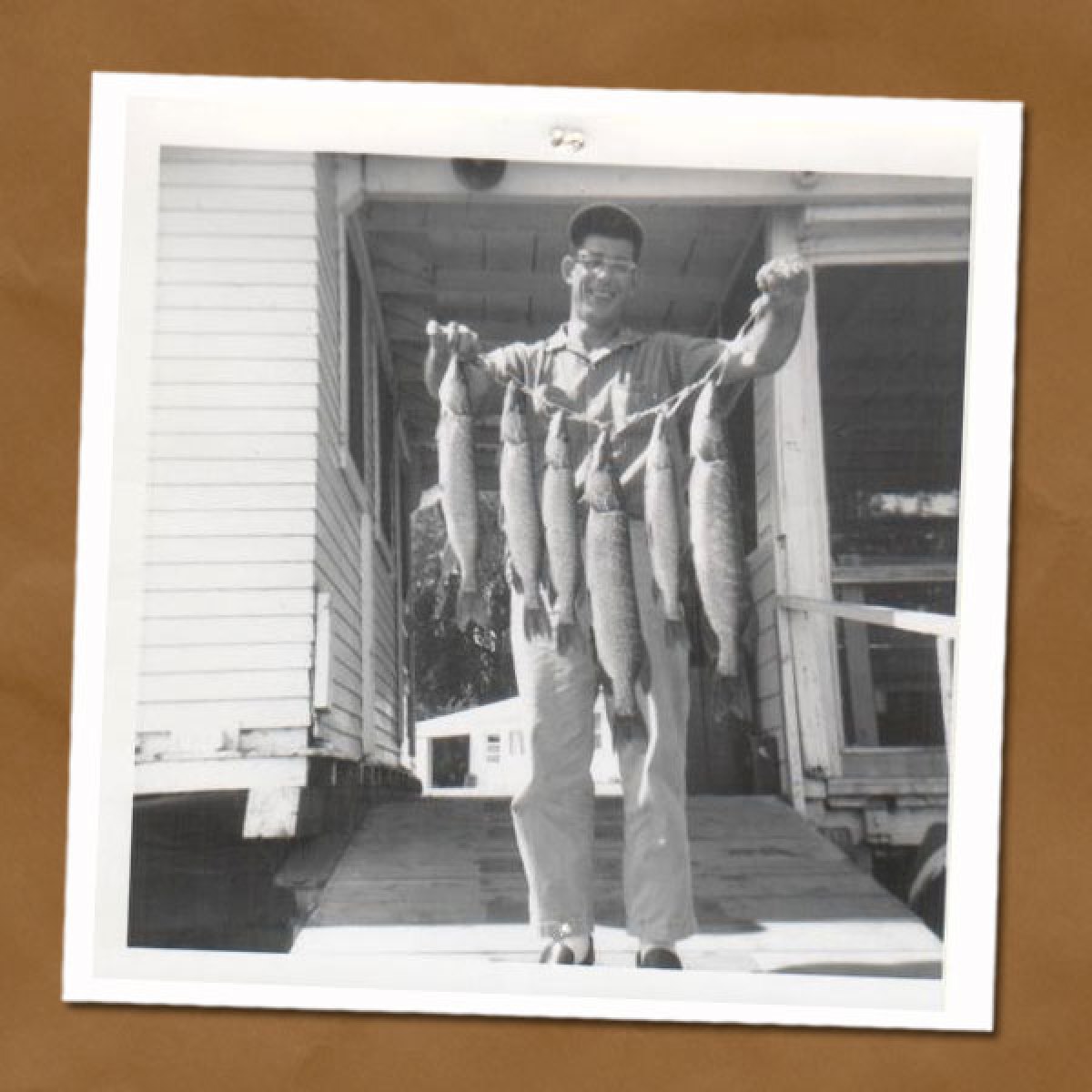 Black and white photo of man holding up string of fish by Tally's Dockside marina