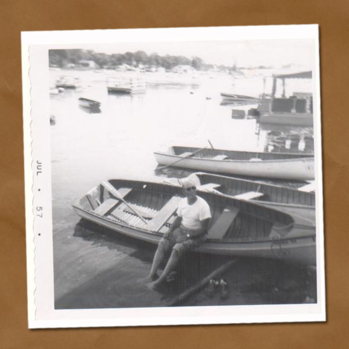 Black and white photo of man leaning against old boat pulled onto shore